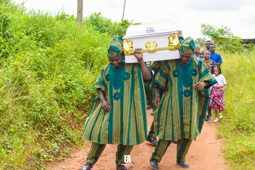 Pallbearers in green traditional attire carrying a white casket with gold handles in a procession
